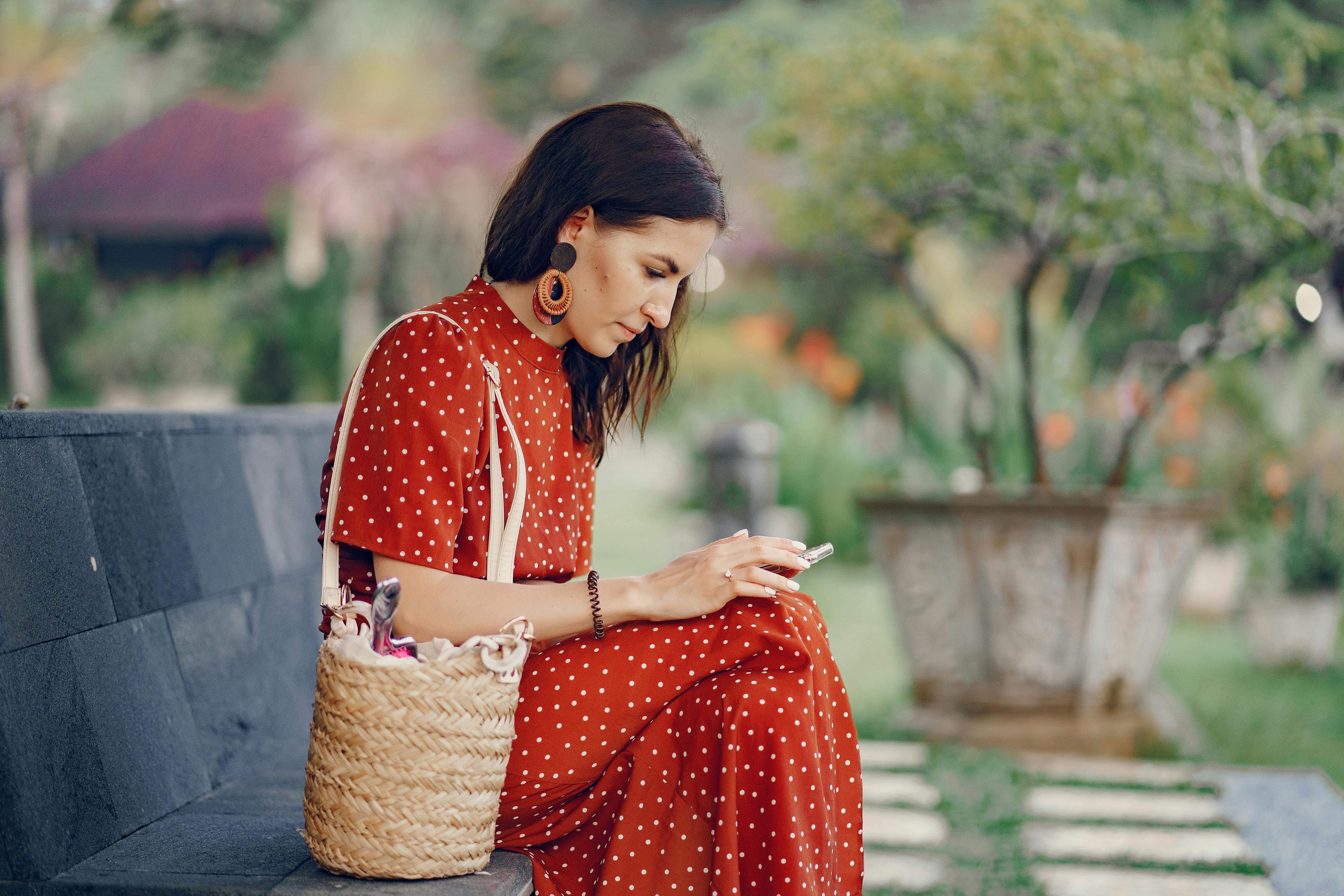 good app design woman in red dress in a park on a bench scrolling phone