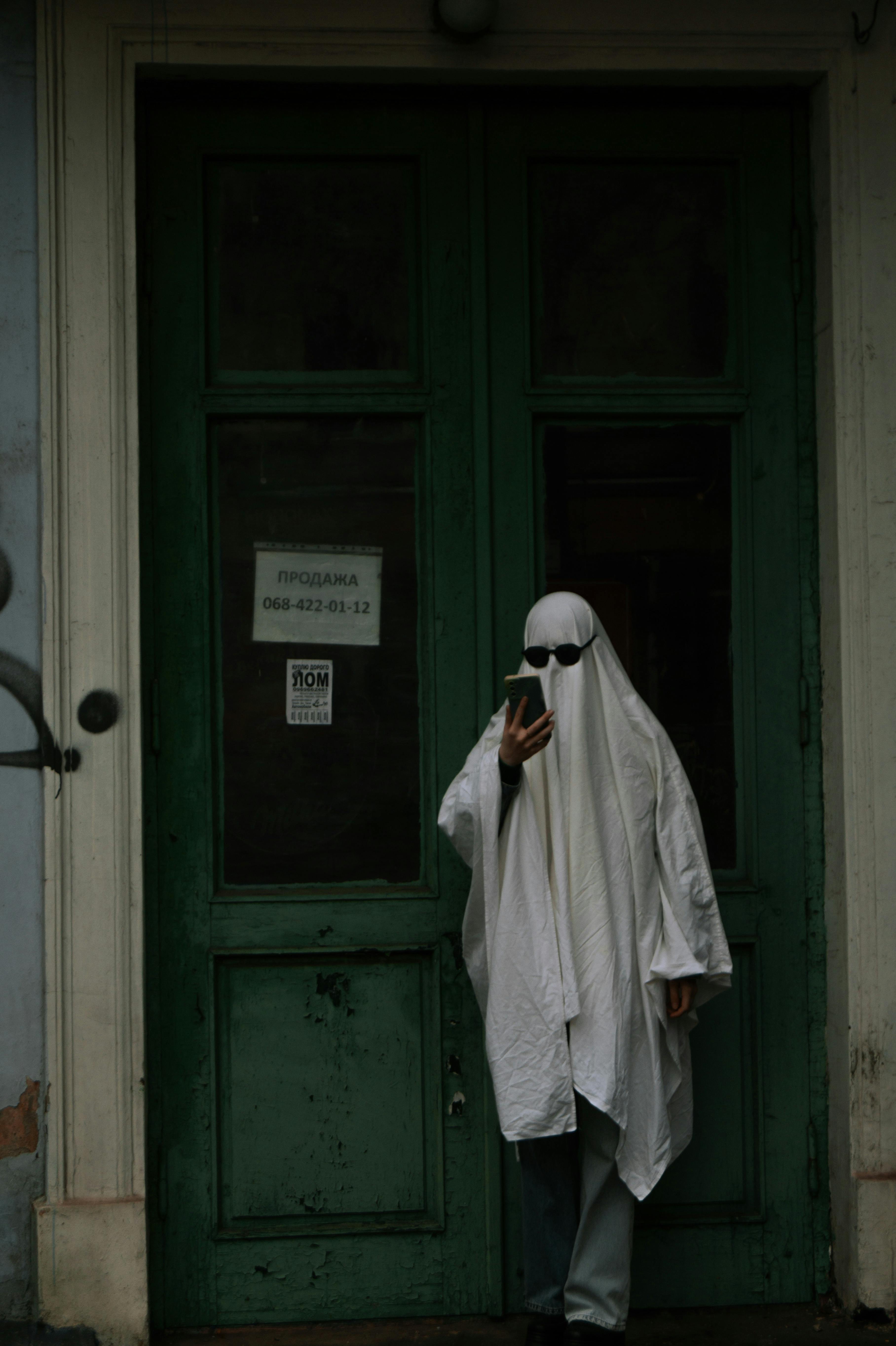 halloween ghost with sunglasses and phone next to a green door