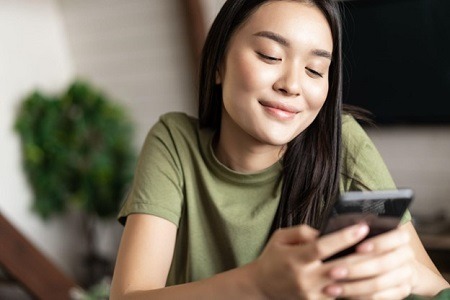 asian wonan in green tshirt looking at her phone smiling